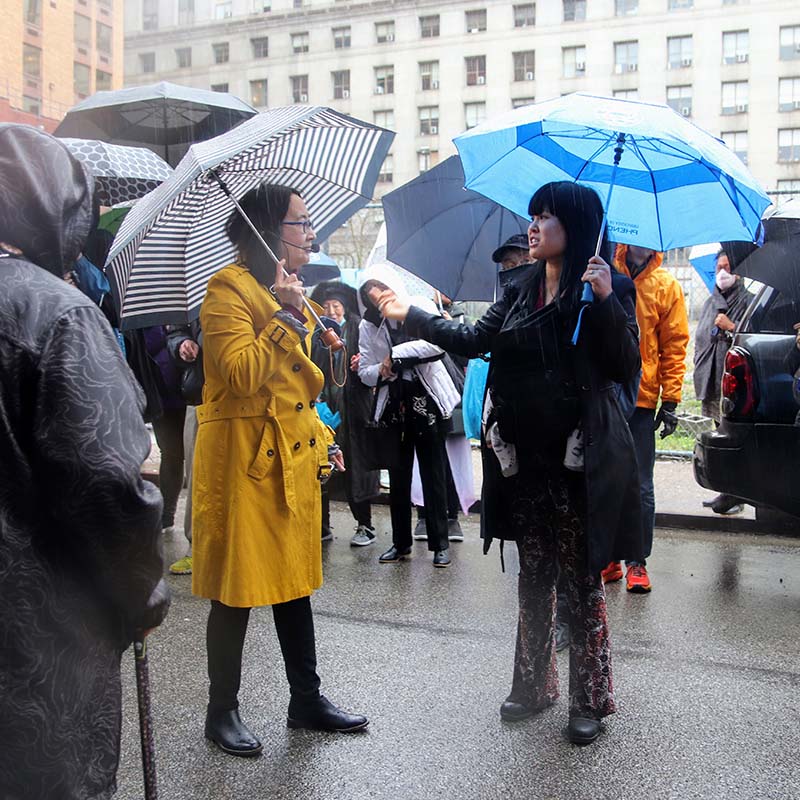 Two women, both with umbrellas, in an urban setting.