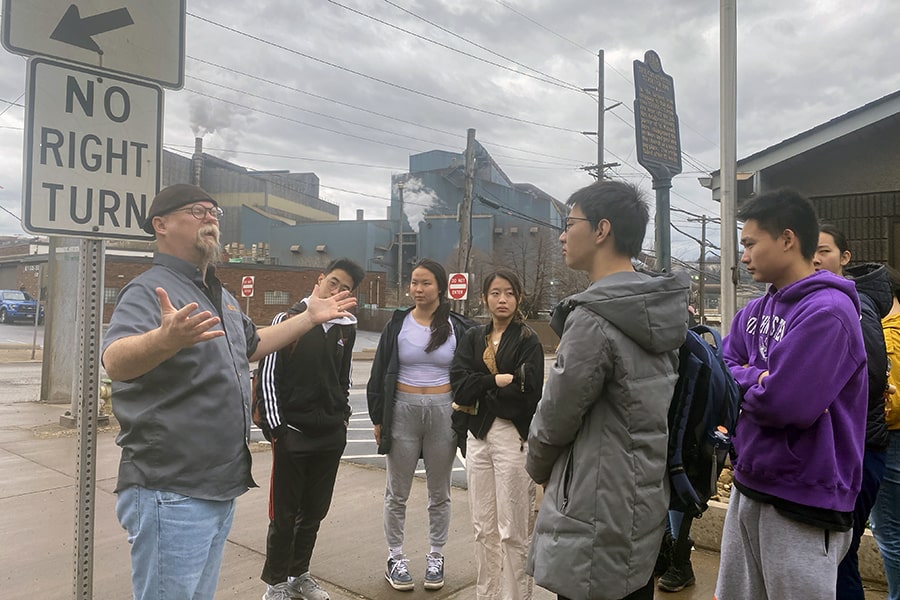 an instructor speaks to students while they stand on a city sidewalk