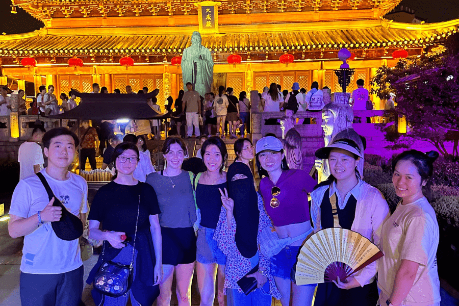 Group of students pose in front of a lit-up building in Shanghai, China at night.