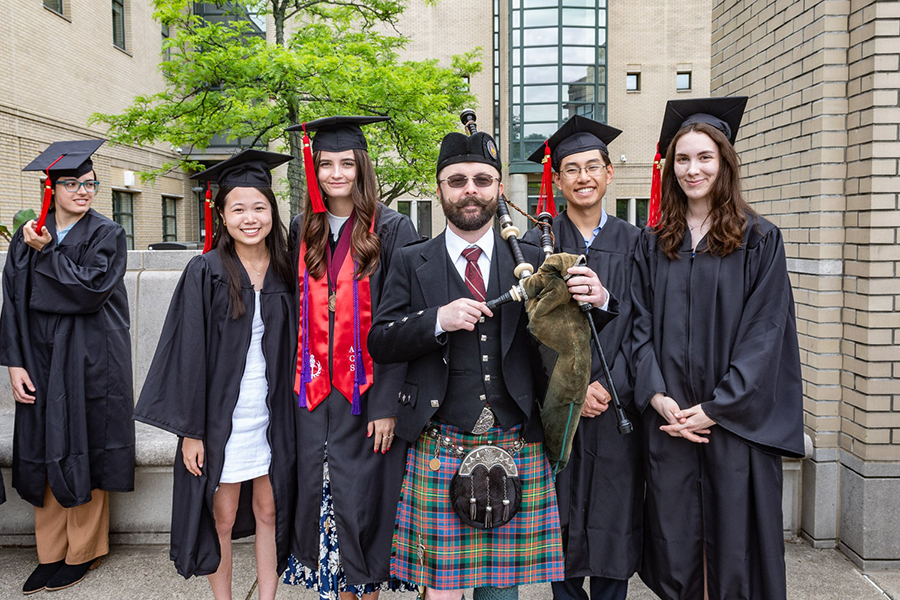 Four PBK inductees in regalia pose with a bagpiper in a kilt.