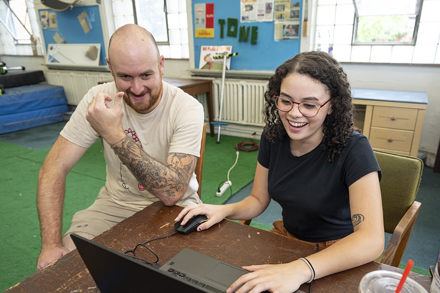 Zoë Brown and Will Weiner are sitting next to each other, smiling, having a conversation about the project Zoë is working on.