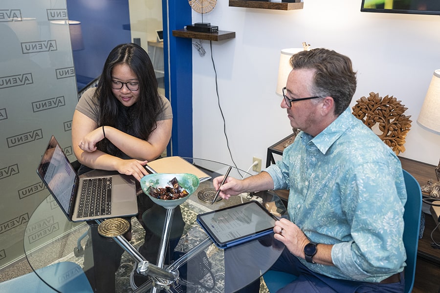 Vionnie Kong and Shawn Fertitta sit next to each other, conversing about a project Vionnie is working on, while looking at Vionnie’s computer.