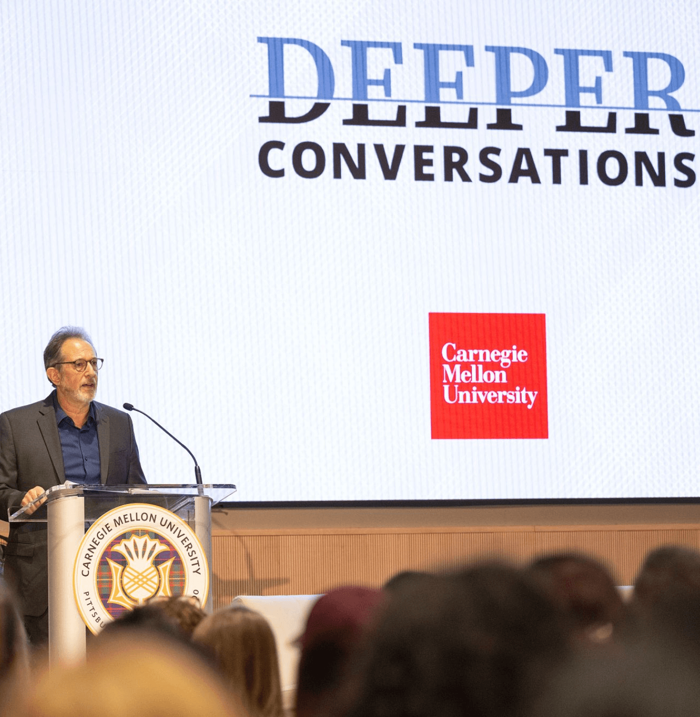 Dean Scheines speaking at the podium during a Deeper Conversations event