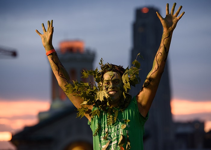 a student dressed in green with their hands in the air