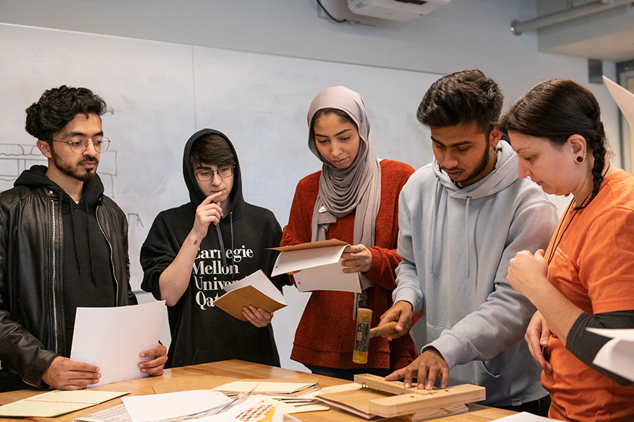 Students from Carnegie Mellon University Qatar around a table, looking at papers and a physical model.