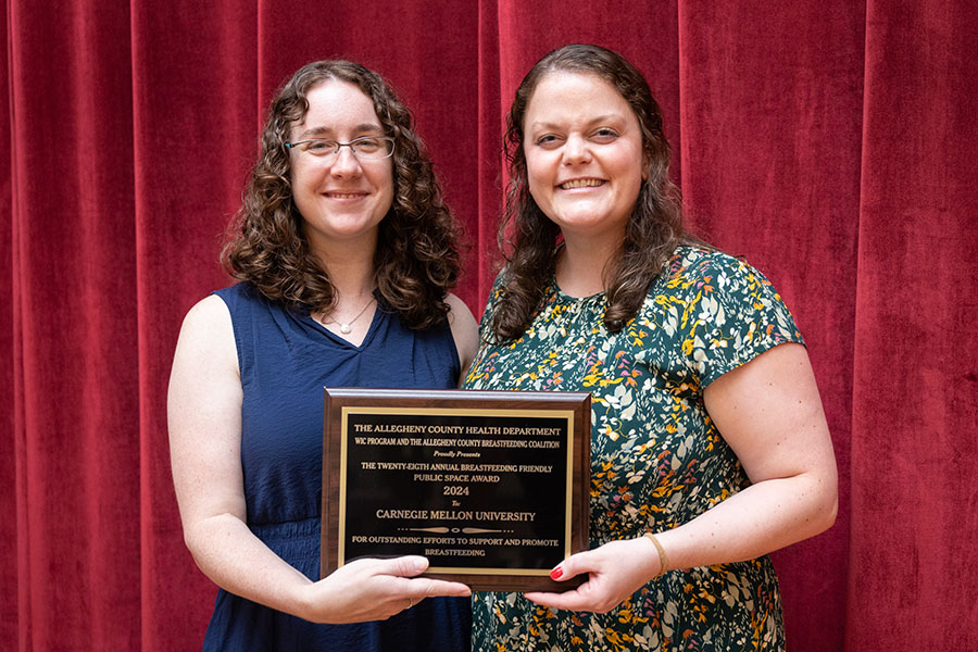 Becca Naughton and Jaimie Schoyer from the CMU Family Care team holding award and posing in front of red velvet curtain