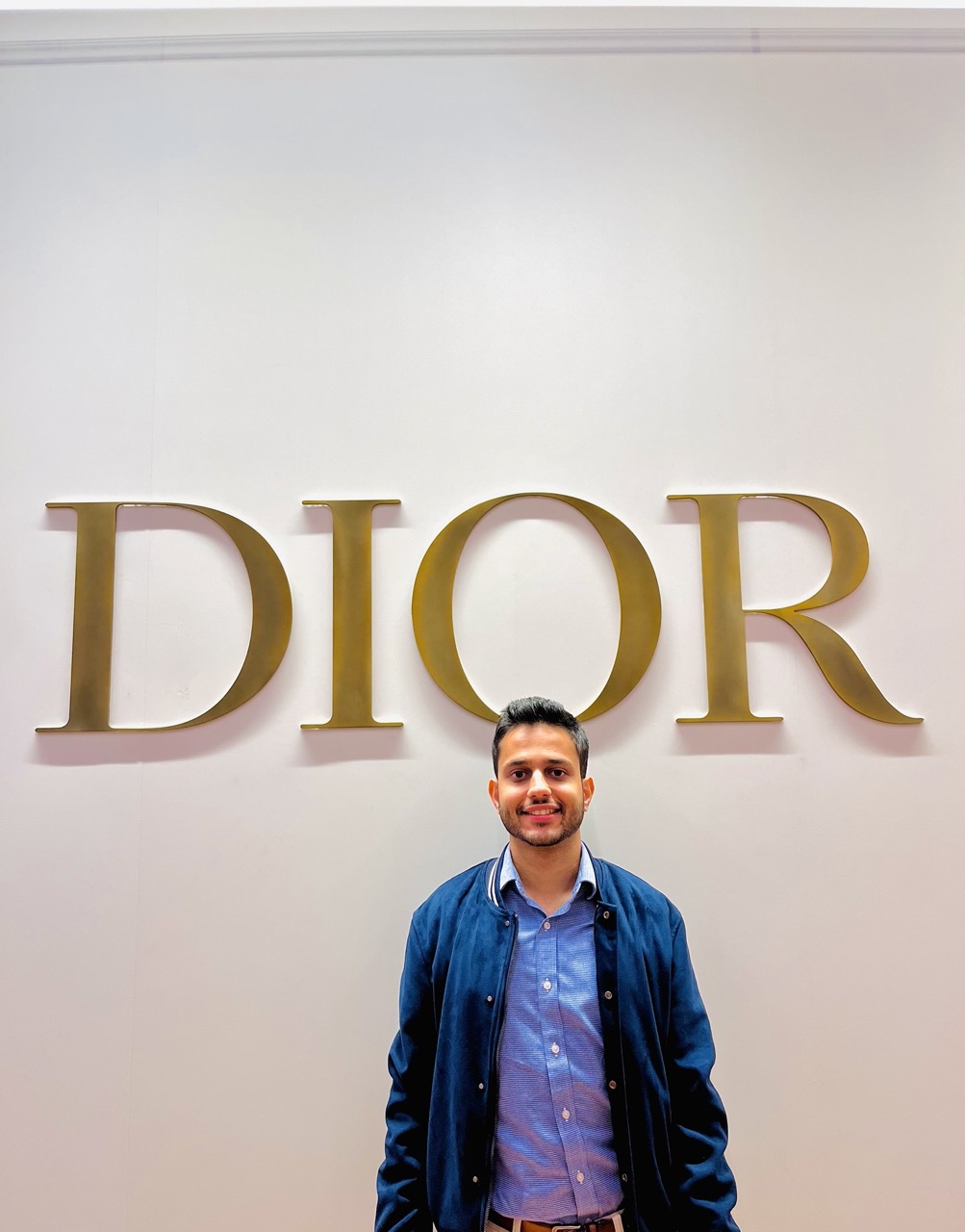 student ambar kakkar stands in front of the Christian Dior logo at his internship