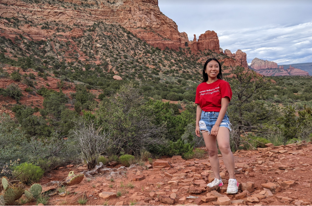 student nini hong is pictured in front of a beautiful landscape of a tall canyon filled with green brush in Arizona