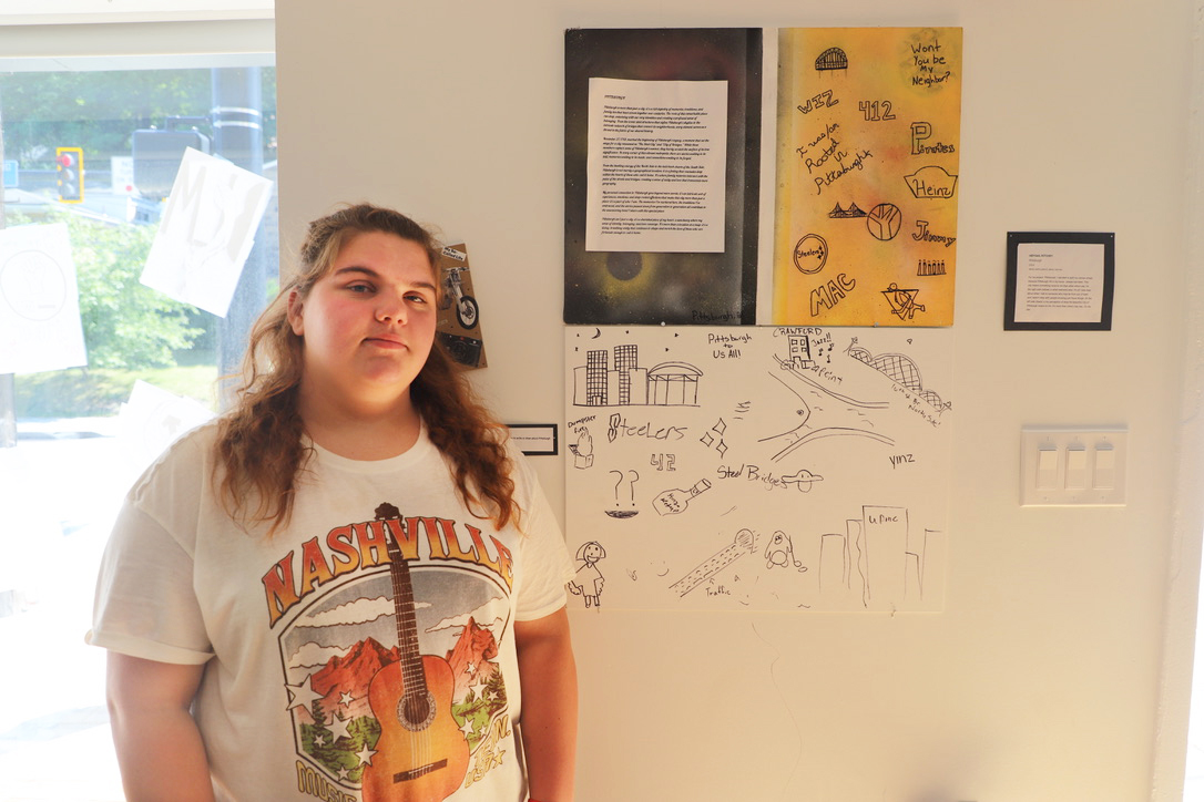 LEAP student, Aby, standing next to a spray painted canvas that she created