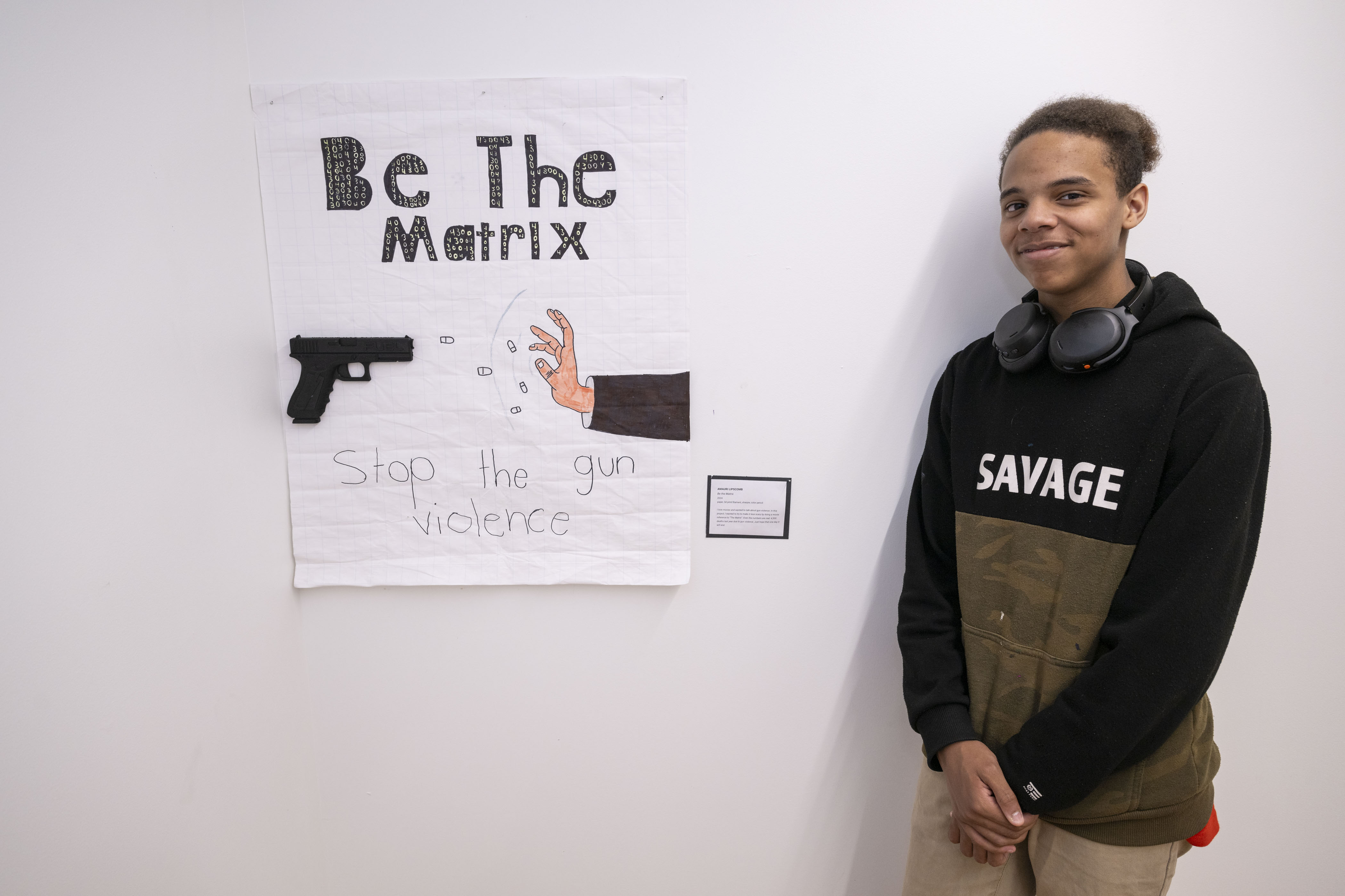 LEAP student, Amauri, standing next to a poster he drew with a 3D printed model of a gun attached to it.