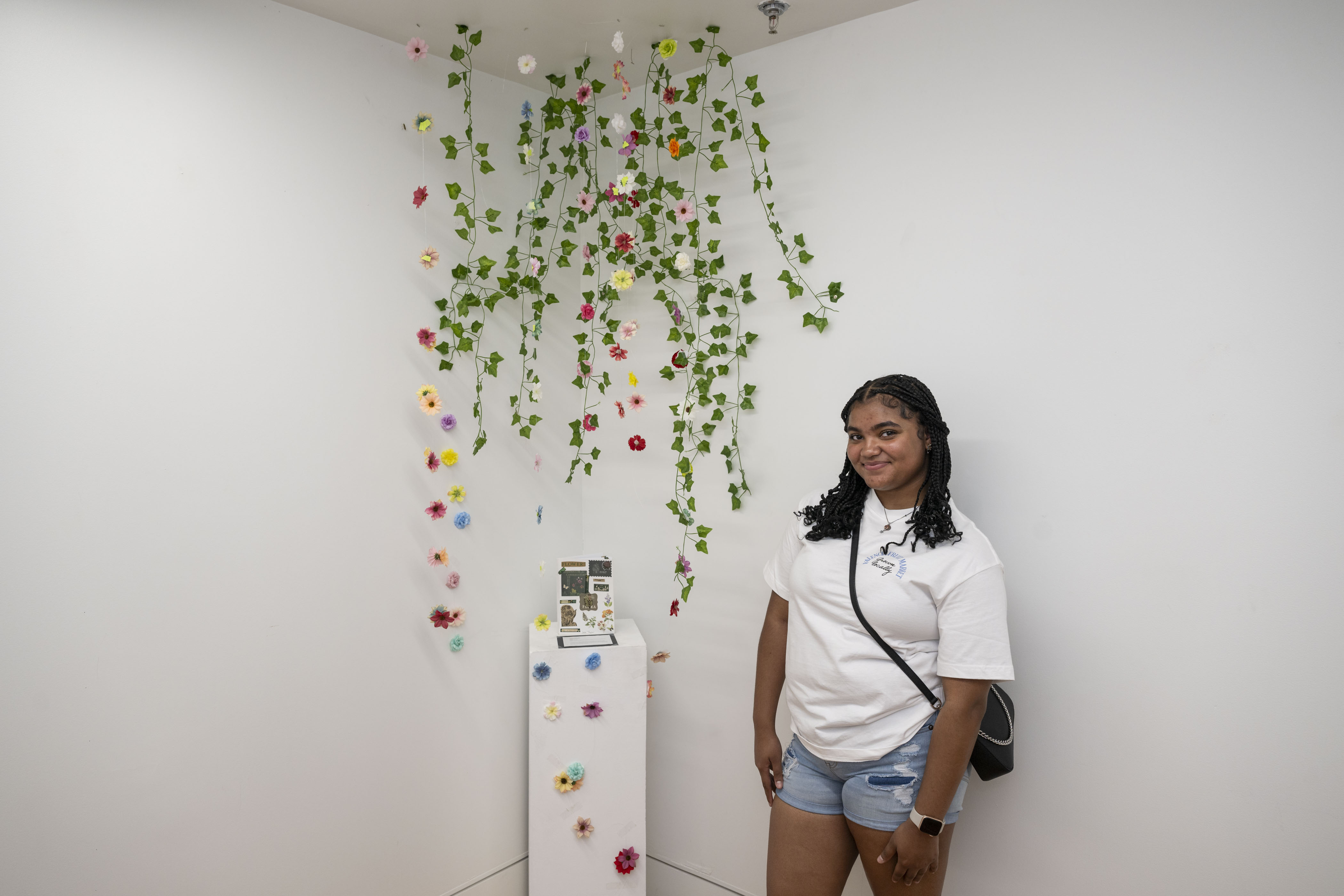 LEAP student, Jada, standing next to an installation of faux flowers and vines hanging from the ceiling and surrounding a book she created