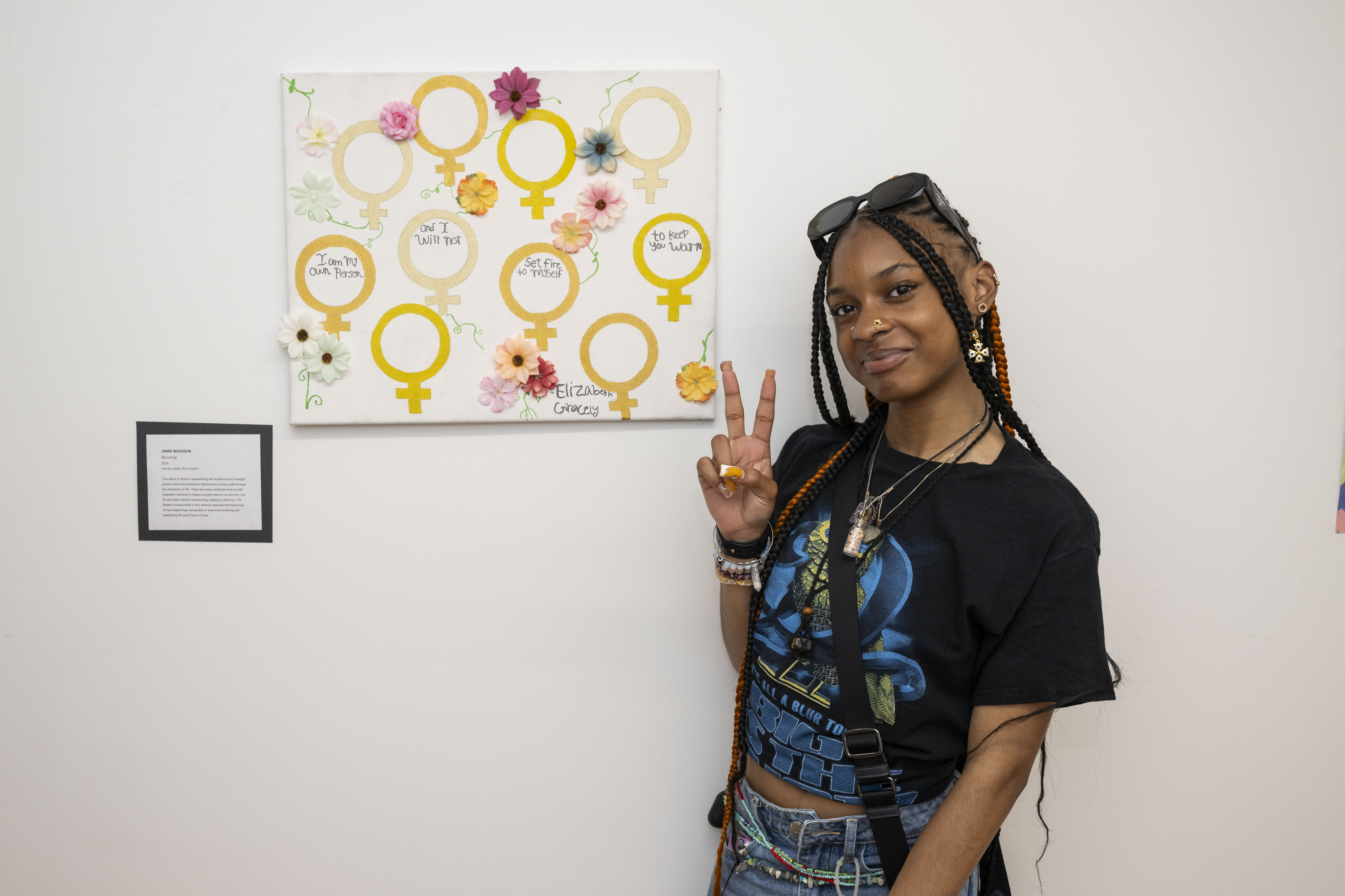 LEAP student, Jamie, standing next to a painting she made with gold paint and faux flowers