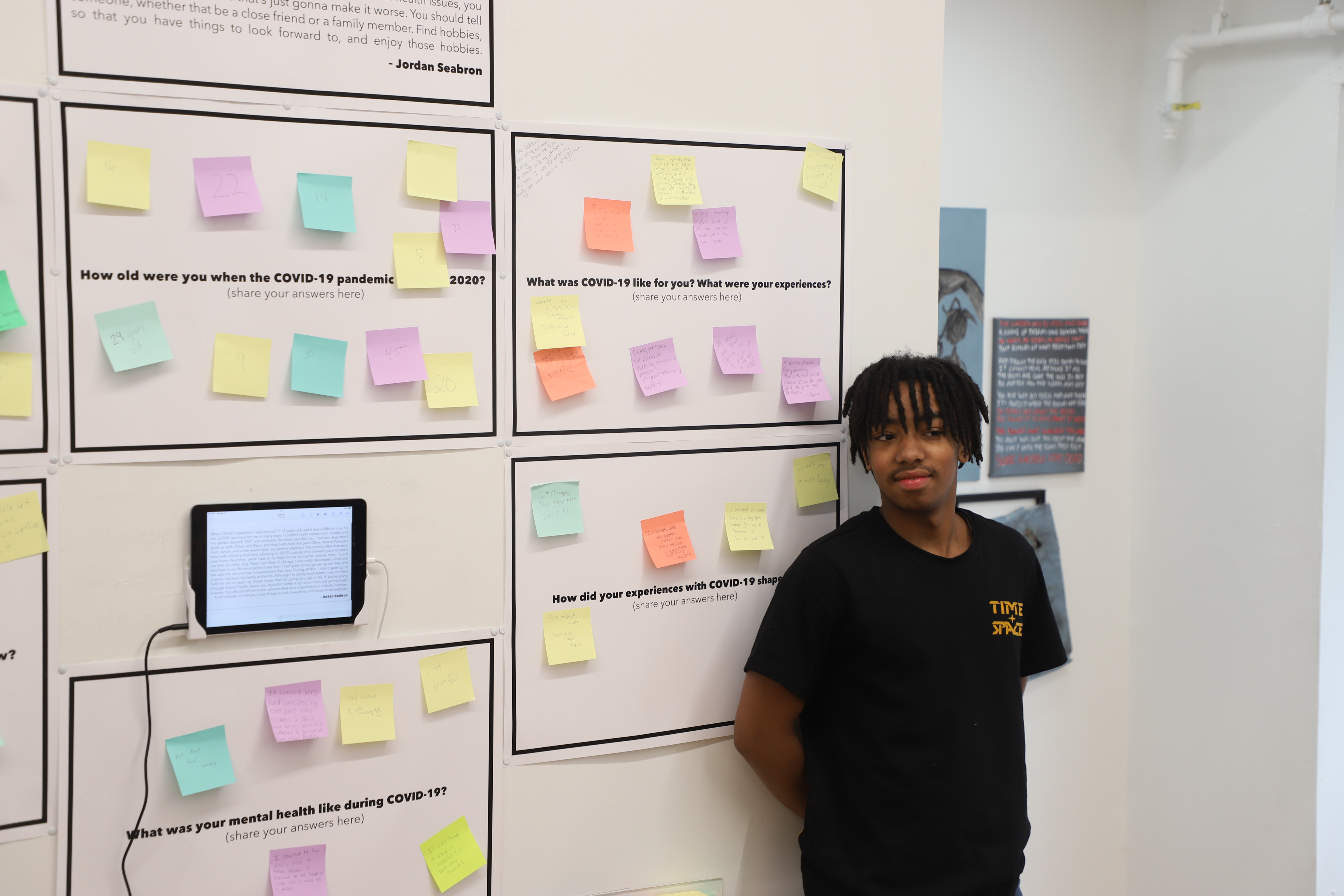 LEAP student Jordan standing next to a series of posters with post-it notes and an iPad playing an audio piece he created