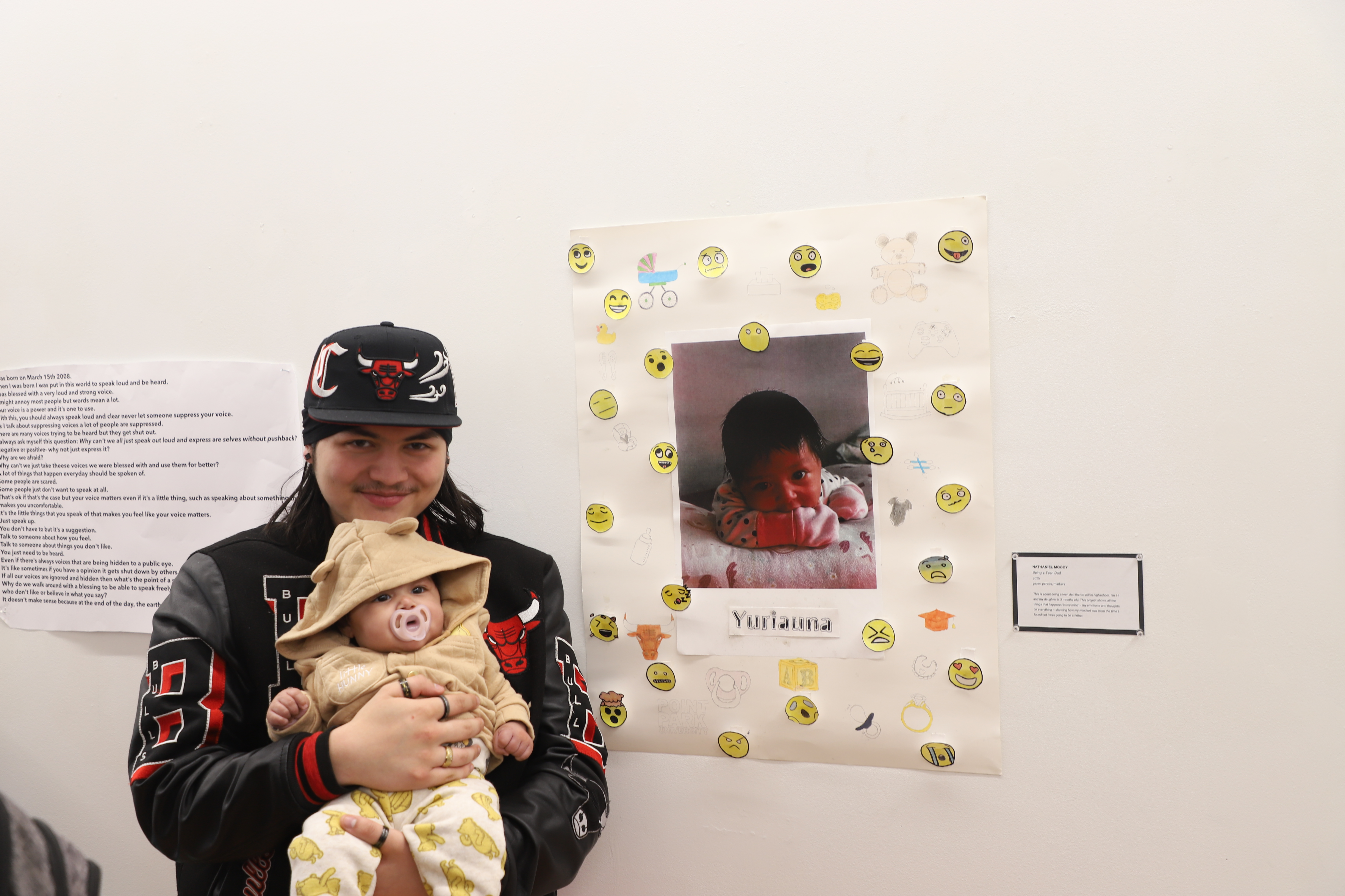 LEAP student Nate holding his daughter and standing in front of a collage and drawing he created