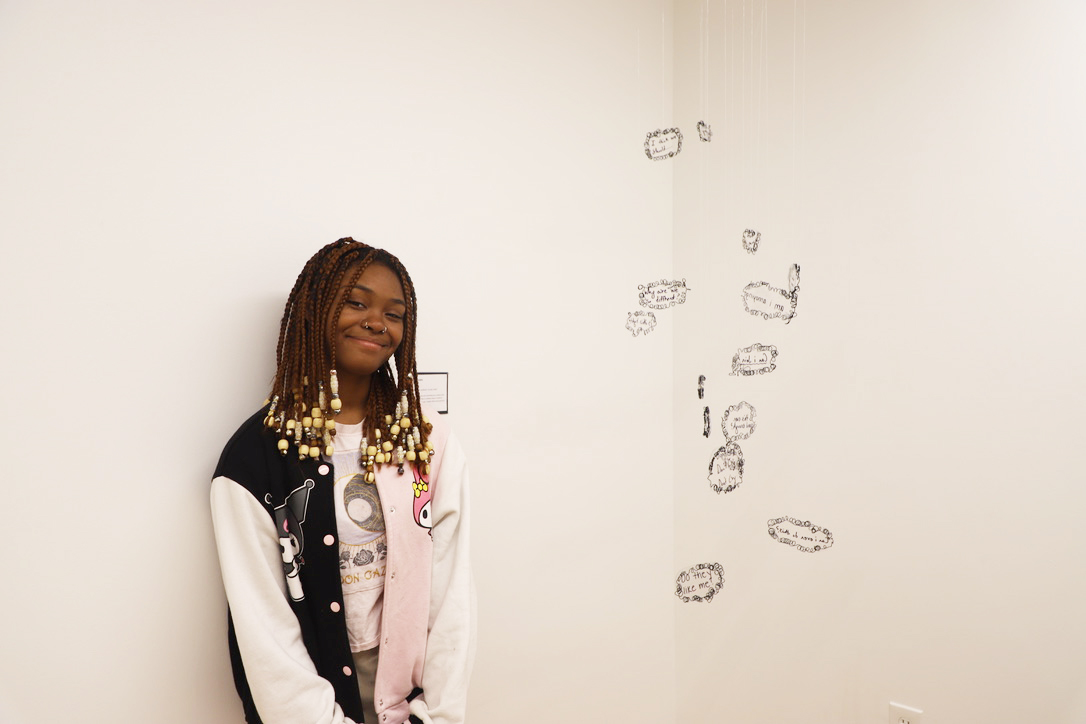 LEAP student, Taleijha, standing next to an installation she created by hanging plastic thought bubbles from the ceiling with fishing line