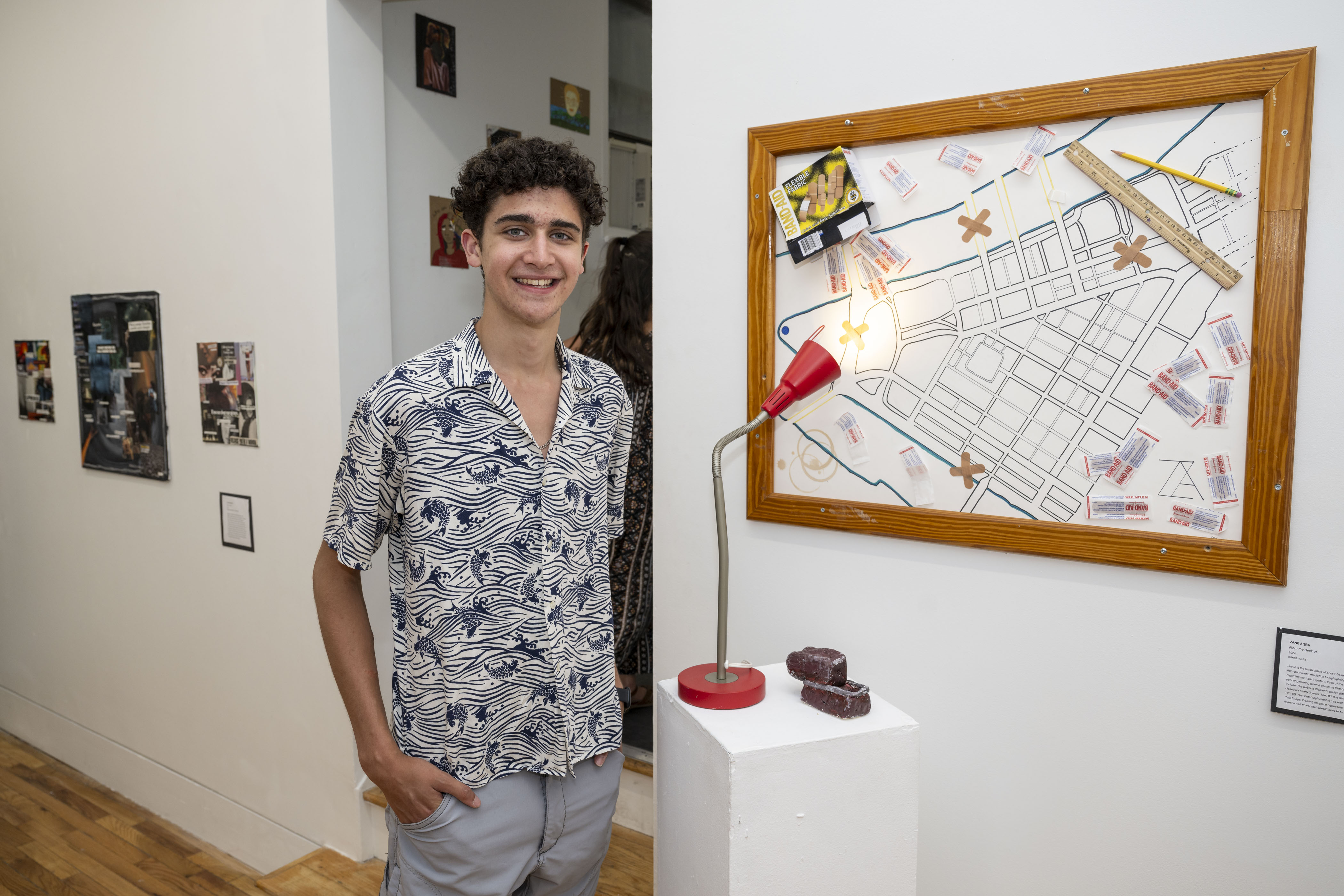 LEAP student, Zane, standing next to an installation he created by framing a large drawing behind a small clay sculpture and a found lamp