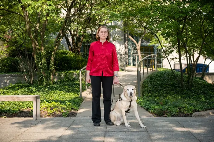 Catherine Getchell standing outdoors with guide dog seated