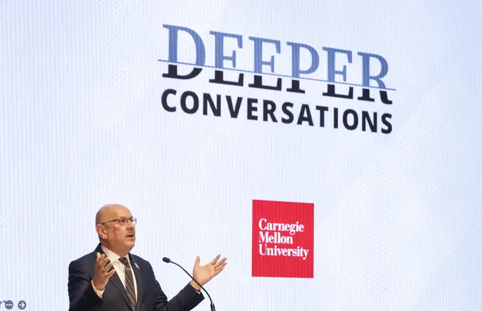 Farnam Jahanian speaks in front of a screen displaying "Deeper Conversations."