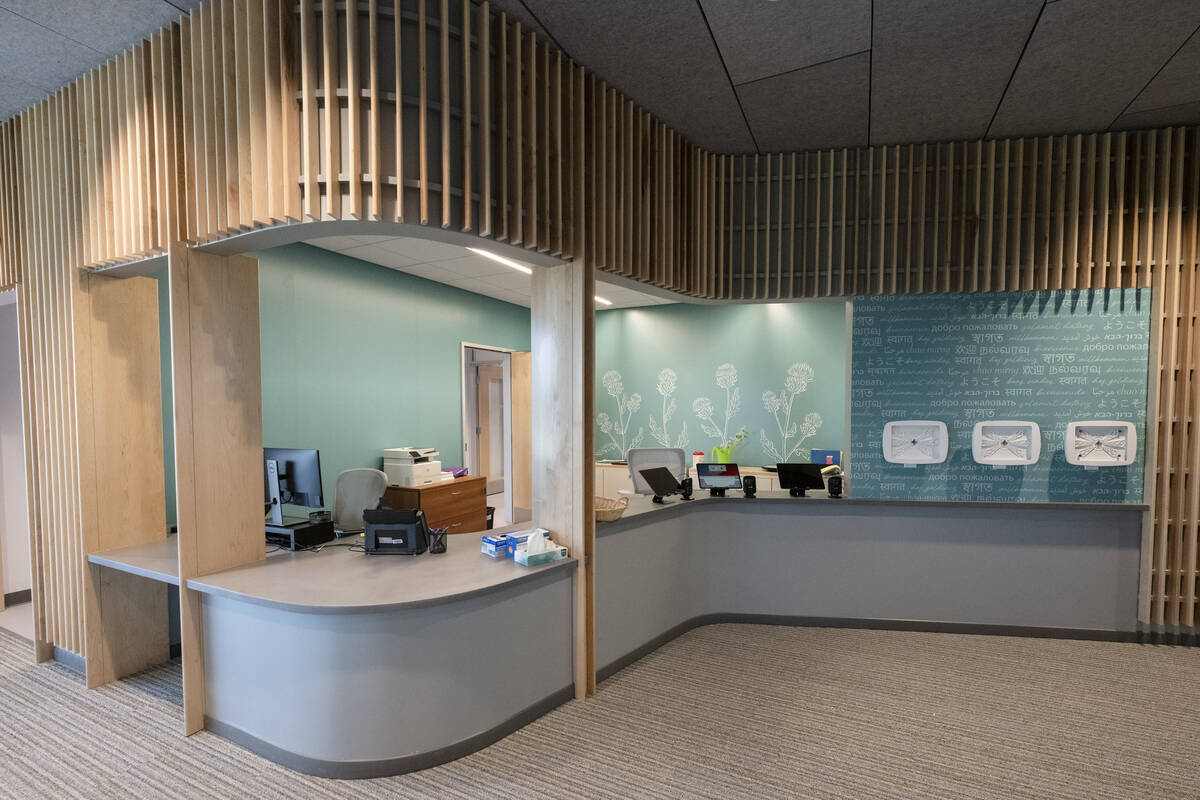 Empty reception counter with thinly spaced wooden vertical slats on the bulkhead above and a teal wall behind where the receptionists would sit.