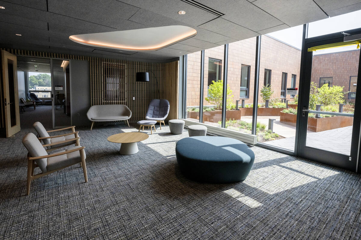 Lounge area featuring modern chairs and couches made of muted gray and purple with light-colored wooden legs sit near a wall of windows looking out into a garden