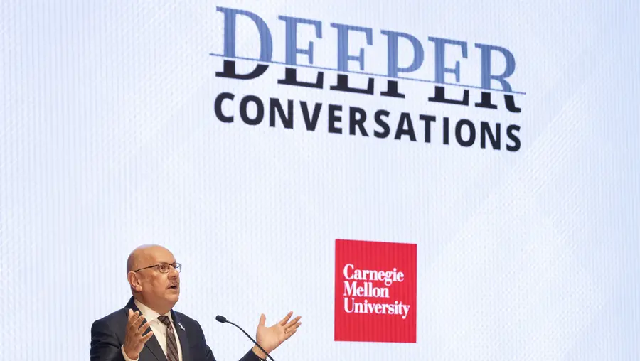 Farnam Jahanian speaks in front of a screen displaying "Deeper Conversations."