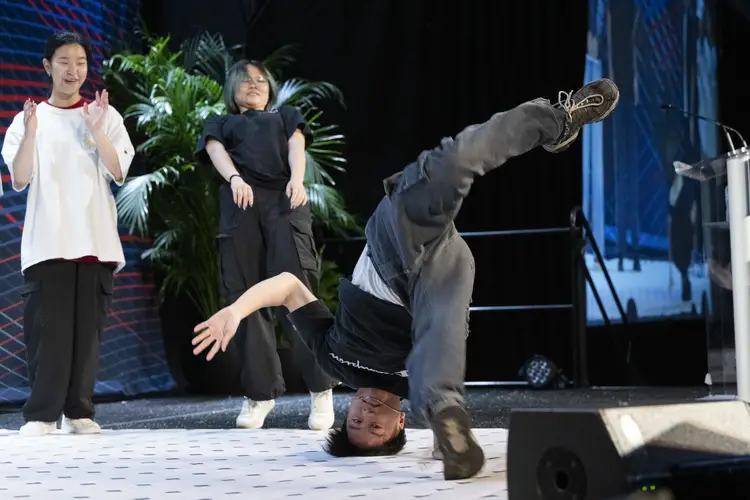 A man spins on his head while breakdancing as two people behind him look on.