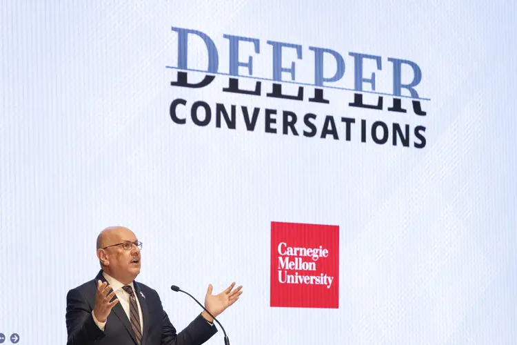 Farnam Jahanian speaks in front of a screen displaying "Deeper Conversations."