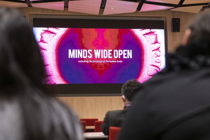 An image of a brainplay lecture session. A projector screen can be seen in front of an audience; the screen says Minds Wide Open.