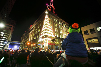 Image of a large Christmas tree made out of lights on the corner of a building and a crowd looking up at it