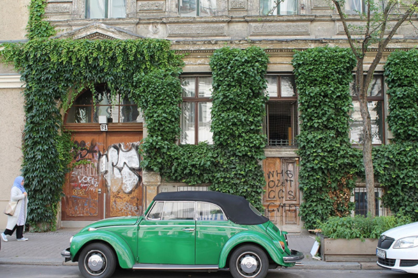 Images of a green antique volkswagen bug car in front of a wall covered in street art
