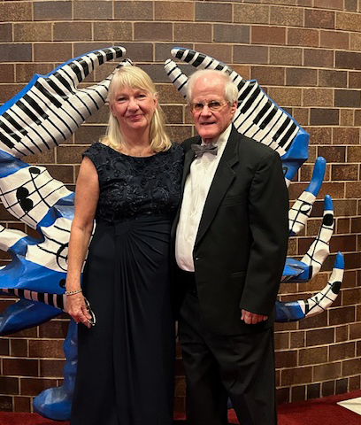 Beth Buck and her husband stand at a gala in front of a blue and white statue in the shape of a crab with music notes on it