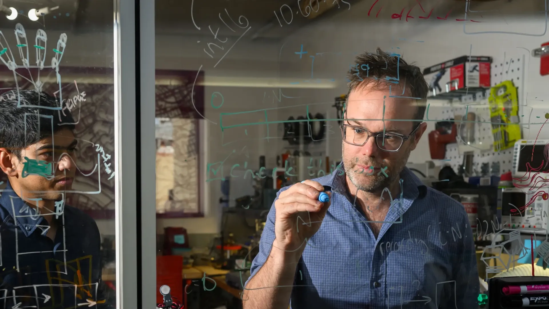 Professor and student writing equations on a window